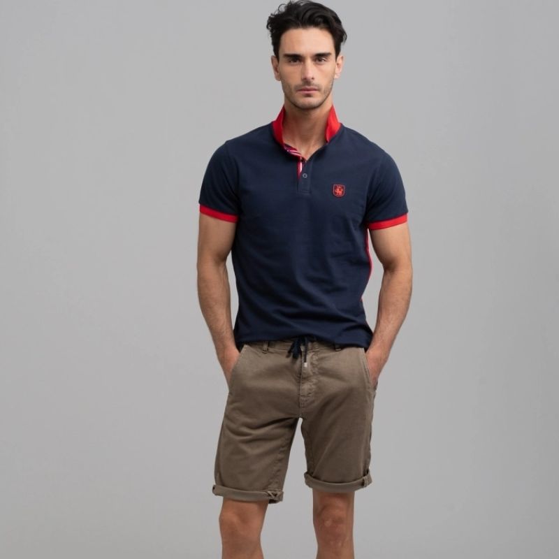 Uomo che indossa polo blu con collo rosso e bermuda in tessuto broken stretch